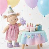Doll with a birthday hat and cake, surrounded by colorful balloons and confetti on a light background