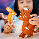 Child holding a toy mouse and a toy Gruffalo creature with a blurred background